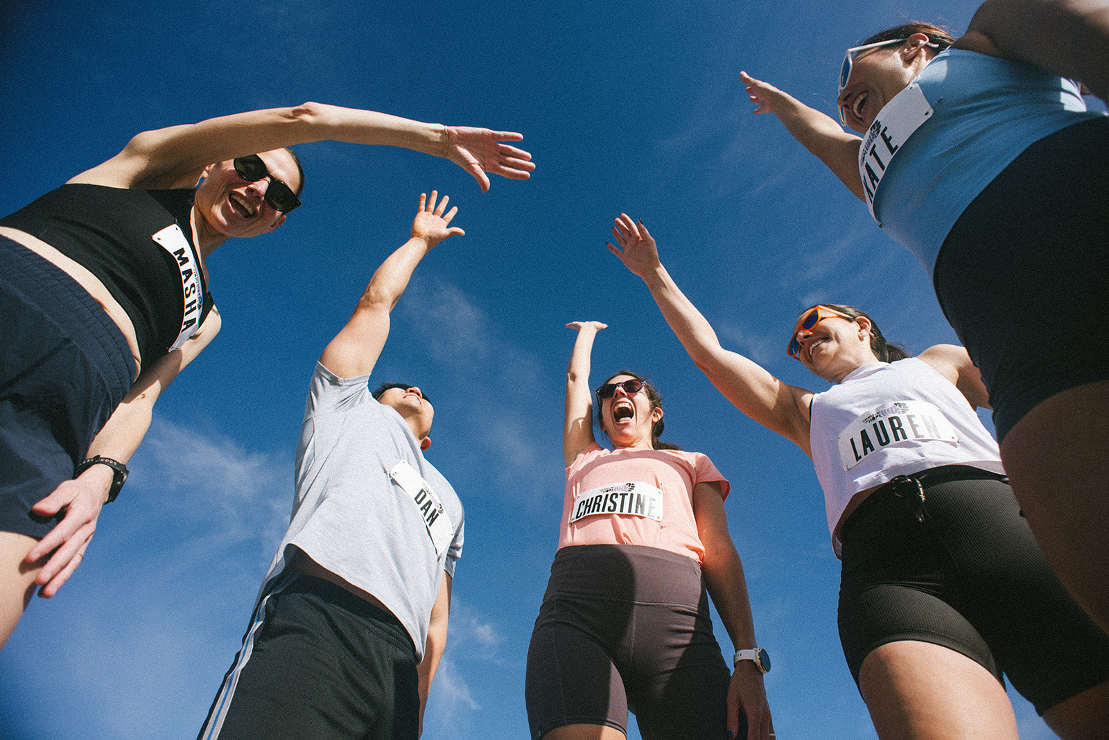 Five runners with arms raised against a blue sky